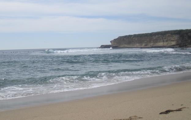 shot from the beach of a distant wave peelng right, away from a bluff